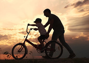 Silhouette of a parent helping a child ride a bicycle at sunset symbolizing Child Support Modifications